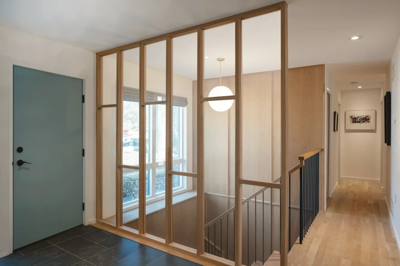 View of new entry foyer and mid-century modern floating stair which includes glass partition wall, white oak paneling, white oak floating slabs and blackened steel picket rail and white oak handrail