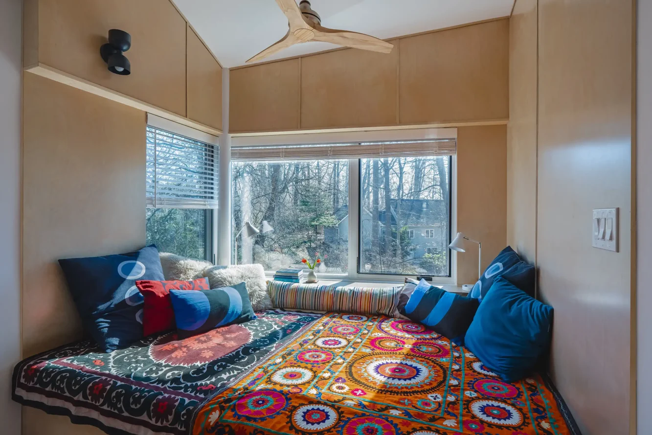 Interior view of cantilevered "treehouse" library reading niche showing wood paneling, super sized lounging daybed with colorful fabrics and pillows