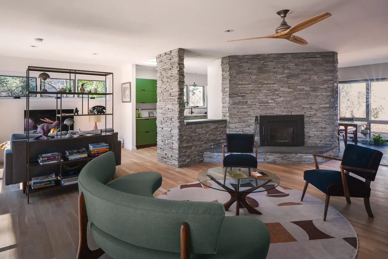 View of existing fireplace and hearth newly clad in stack stone veneer, peek through view of mod kitchen beyond and "snuggery" at left